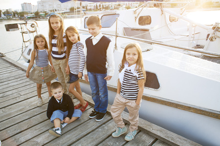 Many fashion kids models wearing navy clothes in marine style walking in the sea port near white fashionable yachtの写真素材