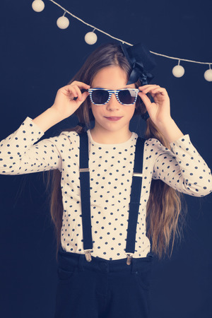 Fashion photo of young hipster child wearing cool clothes and sunglasses standing over dark wall の写真素材