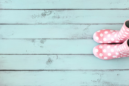 Pink polka dot rain boots on mint blue shabby chic wooden background, top view point