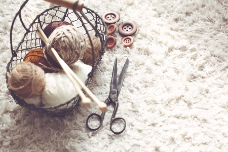 Vintage knitting needles, scissors and yarn inside old wire basket on wooden stool, still life photo with soft focusの写真素材