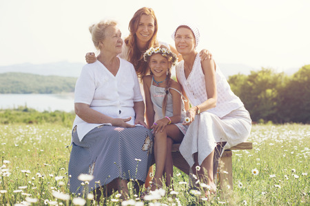 Four generations of beautiful women sitting together in a camomile field and smilingの写真素材