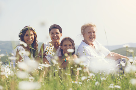 Four generations of beautiful women sitting together in a camomile field and smiling