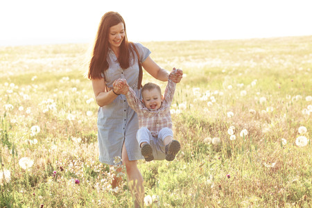 Mother and her child playing in spring field in soft sunlightの写真素材