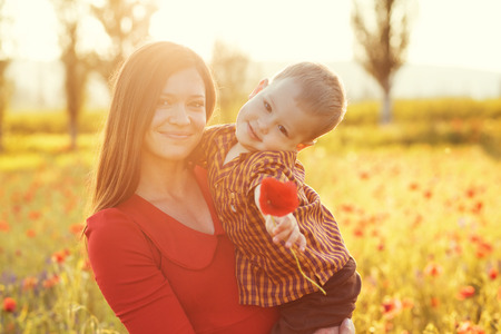 Mother and her child playing in spring poppy field in soft sunlightの写真素材