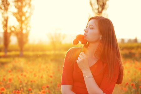 Young woman smelling flower in sunlight in poppy fieldの写真素材