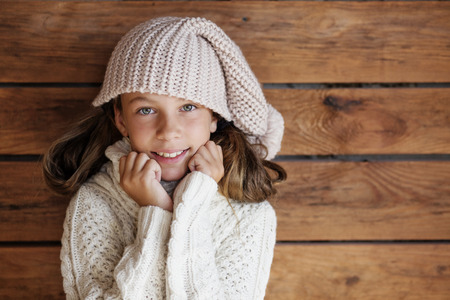 Cute 9 years old girl wearing knitted autumn or winter clothing posing over wooden backgroundの写真素材