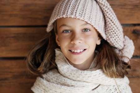 Cute 9 years old girl wearing knitted autumn or winter clothing posing over wooden backgroundの写真素材