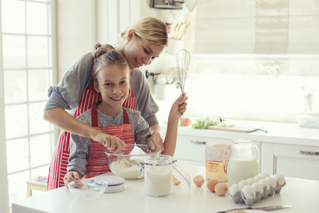 Mom with her 9 years old daughter are cooking in the kitchen to Mothers day, lifestyle photo series in bright home interior