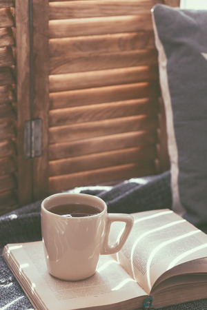 Warm and cozy window seat with cushions and a opened book, light through vintage shutters, rustic style home decor. (Text in the book is not readable, because if was transformed by filter).の写真素材