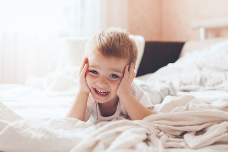 2 years old little boy dressed in pajamas are relaxing and playing in the parent's bed, warm and cozy scene. Pastel colors, selective focus.の写真素材