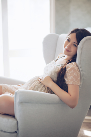 Home cozy portrait of pregnant woman resting at home on a chairの写真素材