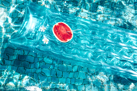 Watermelon on floating mattress in the blue pool. Tropical fruit diet. Summer holiday idyllic.の写真素材