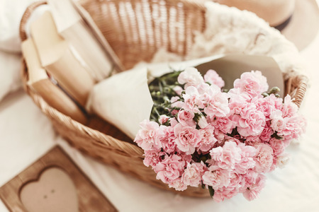 Shabby chic style. Pink pastel flowers in wicker basket on the bed.の写真素材