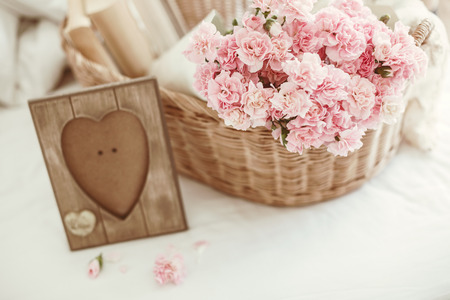 Shabby chic style. Pink pastel flowers in wicker basket on the bed.の写真素材