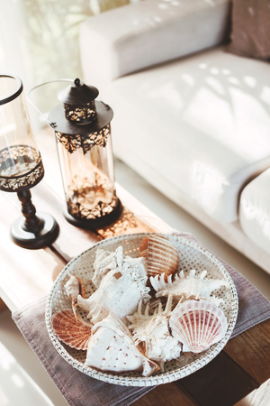 Beach interior decor: sea shells and lanterns on the wooden coffee table, natural colors. Detail of living room.の写真素材
