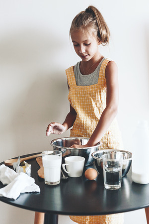 10 years old preteen girl dressed in cotton apron is cooking holiday pie on the table over wall, organic food, lifestyle photoの写真素材