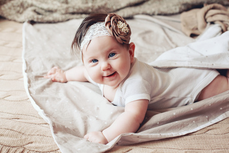 Portrait of a 4 month cute baby girl wearing lace flower headband and lying down on a bed with brown beddingの写真素材