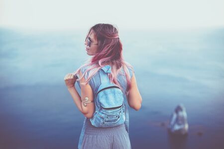 Woman with pink hair standing on the mountain top over blue sea view, photo toned