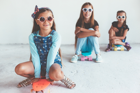 Company of children of different ages wearing cool fashion clothing posing with colorful skateboards against white wall, urban styleの写真素材