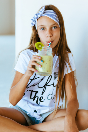 Beautiful teenage girl drinking smoothie shake against white wallの写真素材