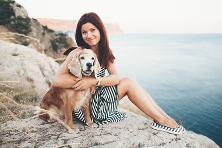 Woman hugs with her dog sitting on mountain over sea view.の写真素材