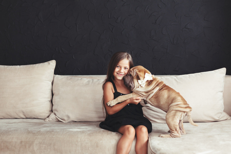 Home portrait of cute child hugging with puppy of Chinese Shar Pei dog on the sofa against black wallの写真素材