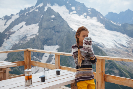 Child standing in the rustick wooden outdoor cafe on mountain, alpine view, snow on hills. Dombay, Karachay-Cherkessia, Caucasus, Russia.の写真素材