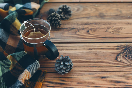 Mug with tea bag and plaid winter scarf on old brown wooden table