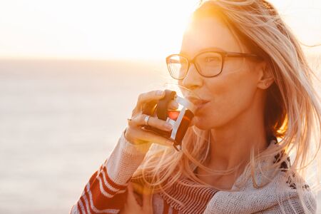 Woman wearing sweater drinking hot tea outdoors in autumn sunlight. Fall cozy concept, backlit.