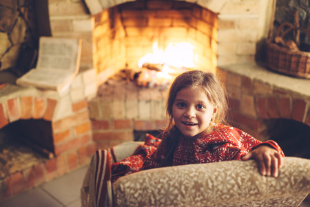 Child in Christmas pajama relaxing by the fire place some cold evening, winter weekends, cozy sceneの写真素材