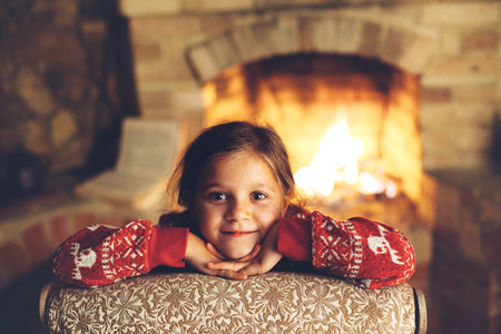 Child in Christmas pajama relaxing by the fire place some cold evening, winter weekends, cozy sceneの写真素材