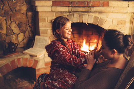 Mom with child playing and chilling by the fire place some cold evening, winter weekends, cozy sceneの写真素材
