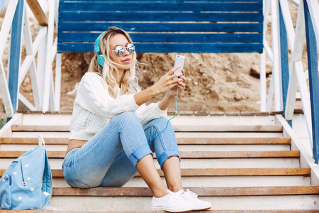 Young woman with backpack wearing sweater and jeans relaxing and listening music at the beach, autumn weekend on the sea shoreの写真素材
