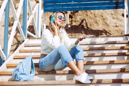 Young woman with backpack wearing sweater and jeans relaxing and listening music at the beach, autumn weekend on the sea shoreの写真素材