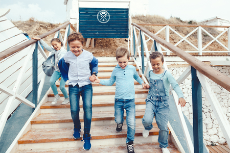 Group of fashion children wearing denim clothing having fun on the sea shore. Autumn casual outfit in blue and navy color. 7-8 years old models.の写真素材