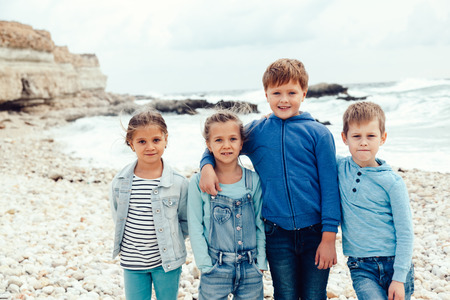Group of fashion children wearing denim clothing having fun on the sea shore. Autumn casual outfit in blue and navy color. 7-8 years old models.の写真素材