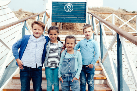 Group of fashion children wearing denim clothing having fun on the sea shore. Autumn casual outfit in blue and navy color. 7-8 years old models.の写真素材