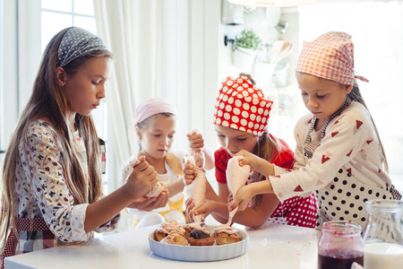 Group of children cooking in the white kitchen. Kids wearing colorful aprons baking dessert at home.の写真素材