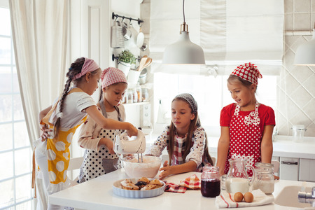 Group of children cooking in the white kitchen. Kids wearing colorful aprons baking dessert at home.