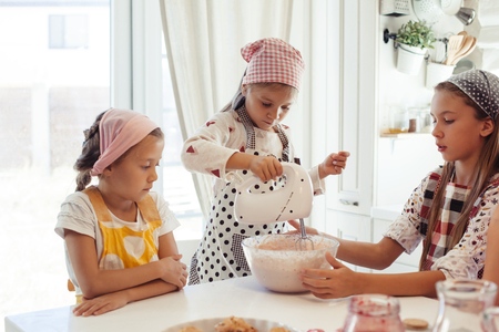 Group of children cooking in the white kitchen. Kids wearing colorful aprons baking dessert at home.の写真素材