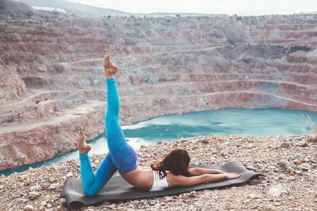 Young sporty girl wearing blue activewear stretching outdoors. Woman training yoga pose on mountain hill, calm and silent view.の写真素材