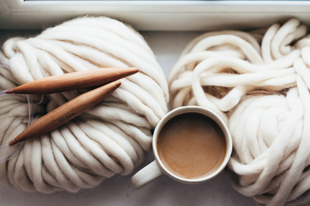 Thick yarn and wooden needles on window sill, top view. Chunky knit. Morning coffee in lazy winter weekend.の写真素材