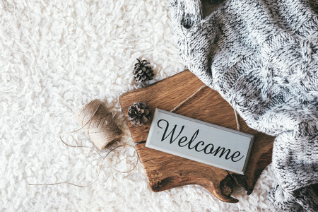 Winter homely scene, scandinavian style. Warm knit blanket and other decor on wooden tray. Craft sign board Welcome. Cafe or home interior decoration.の写真素材