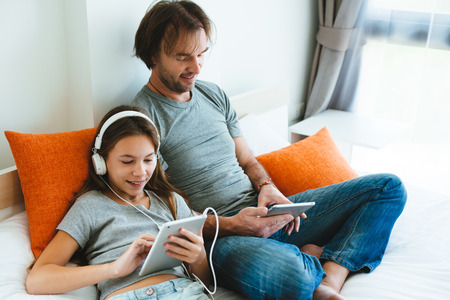 Father and pre teen daughter playing on tablet together on couch in room at home. Good parent and child relations.の写真素材