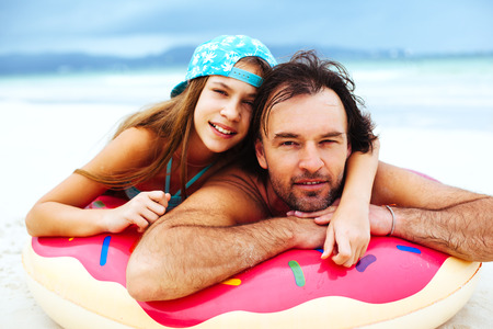 Dad playing with his tween daughter on the inflatable ring on the tropical beachの写真素材