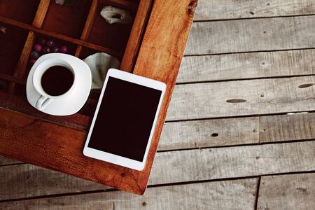 Cup of morning tea or coffee and tablet with blank screen on the wooden table over porch deck. Top view.の写真素材