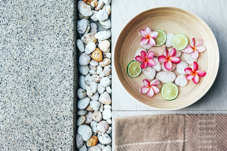 Foot bath in bowl with lime and tropical flowers, organic spa pedicure treatment, top view.