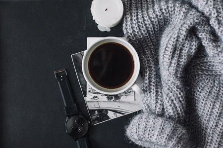 Winter cozy concept. Flatlay of gray knitted sweater, candle and coffee drink on black iron table. Warm weekend in cold weather.の写真素材