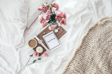 Wooden tray with tablet, coffee and spring flowers on clean white bedding. Good morning concept.の写真素材