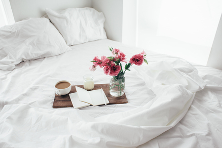 Wooden tray with paper sketchbook, candle and spring flowers on clean white bedding. Good morning concept.の写真素材